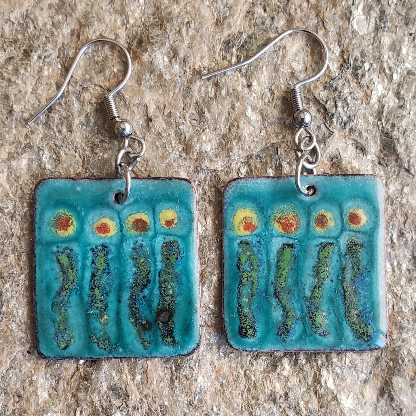 Pair of boho copper enamel earrings with artistic floral design on a textured surface
