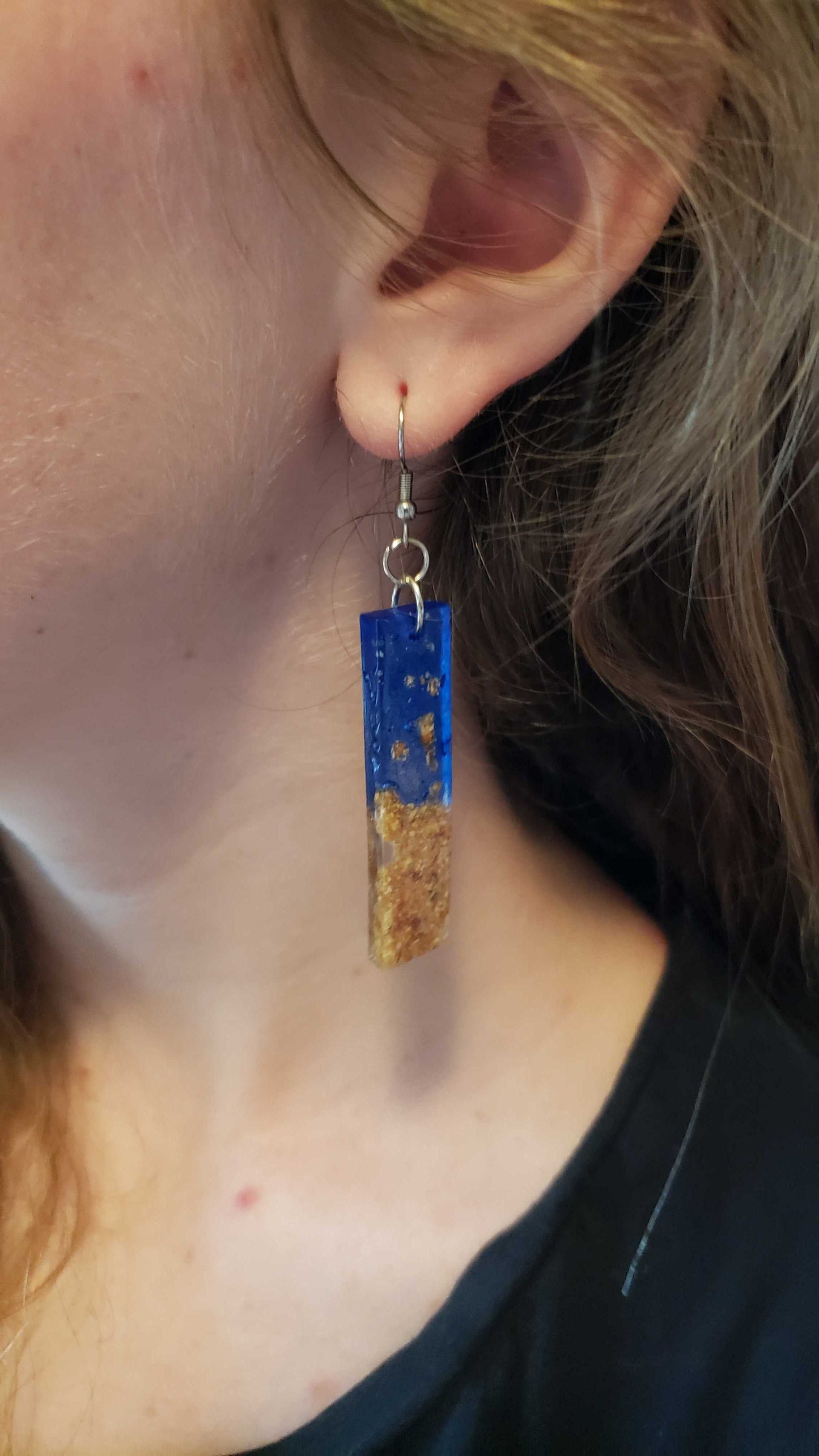 Close-up of a person wearing blue and gold earrings made from dried leaves.