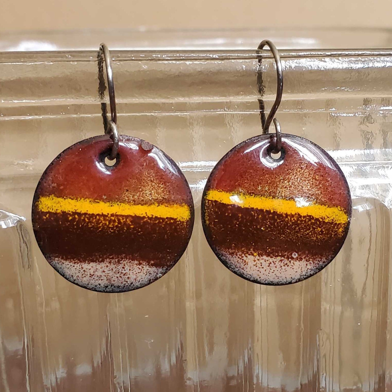 Round  copper earrings with a yellow stripe on a glass jar